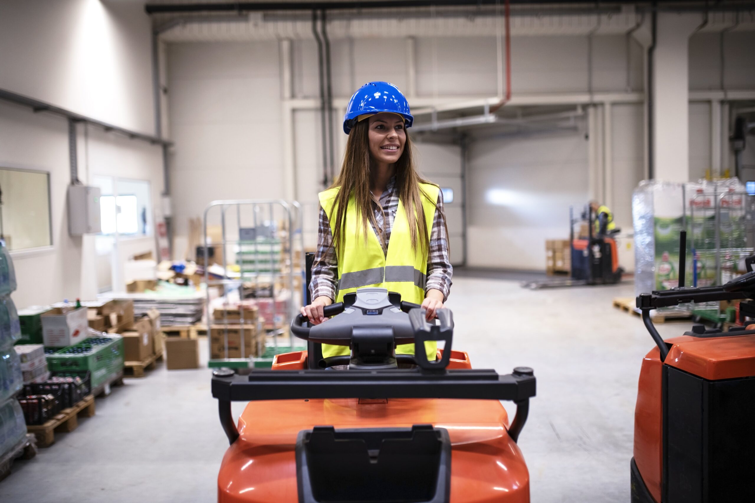 woman-warehouse-worker-with-hardhat-reflective-safety-equipment-driving-forklift-machine-large-distribution-warehouse-center-scaled.jpg